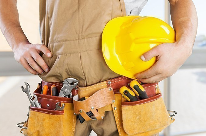 Handwerker mit gelbem Schutzhelm und Werkzeuggürtel, bereit für den Einsatz auf der Baustelle.