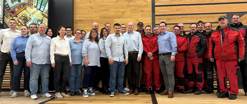 Mitarbeiter-Team im Showroom vor Holzpaneelen und Parkettmustern.
