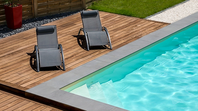 Poolterrasse mit Ipe-Holzdielen, zwei Sonnenliegen und modernem Randabschluss aus Beton, umgeben von Rasen und Gartenzaun.