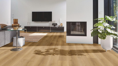 Wohnbereich mit modernem Designboden in warmer Eichenoptik, kombiniert mit Kamin, grauem Sofa und großen Fensterflächen.