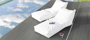 Elegante Poolterrasse mit dunklem WPC-Belag, zwei weißen Lounge-Liegen und ruhiger Wasserreflexion.
