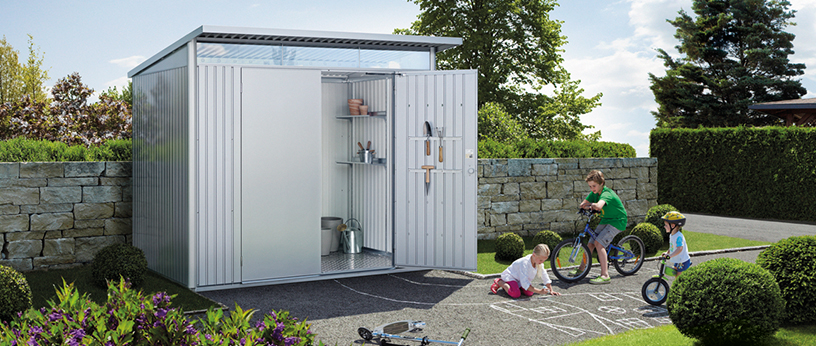 Modernes Metall-Gerätehaus im Garten, innen ordentlich eingerichtet. Kinder spielen davor auf gepflastertem Weg.